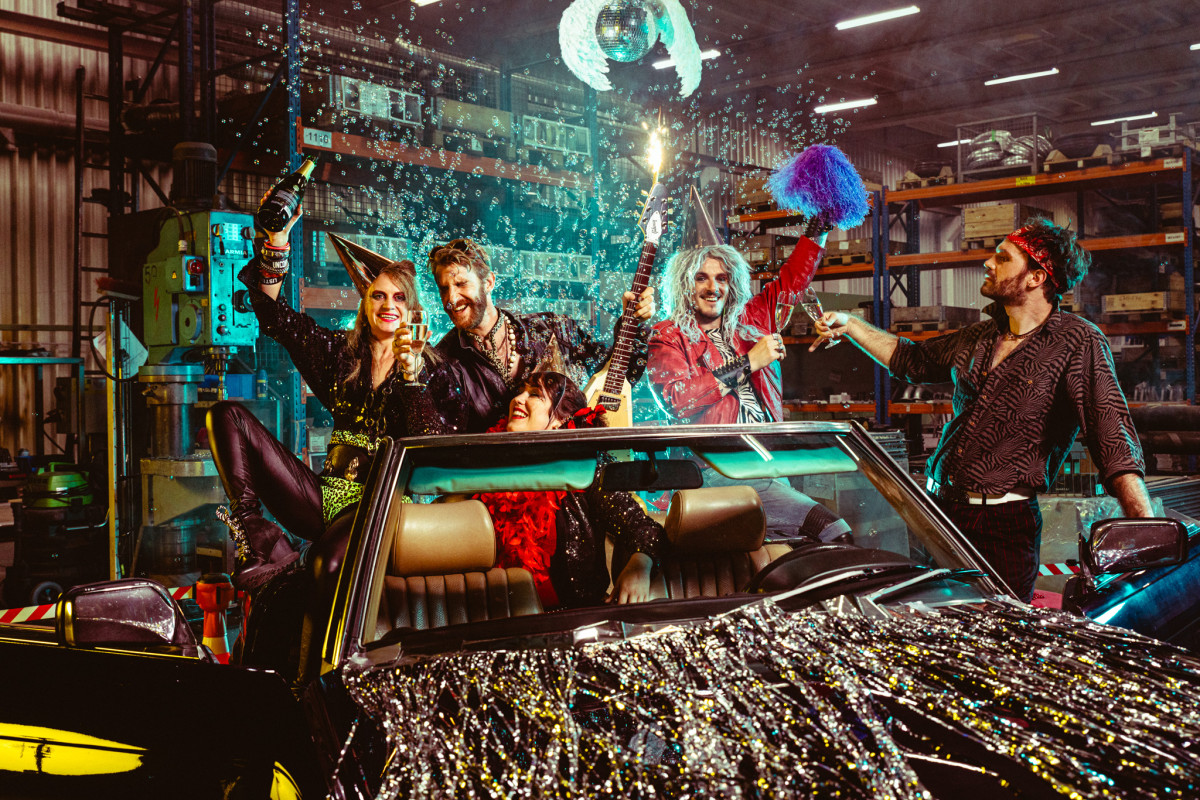 Group picture of 80's cover band Radio Spandex celebrating in convertible car with champagne and firework