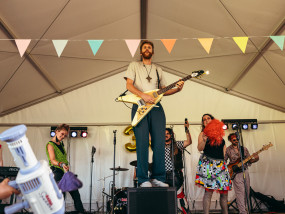 Ctp. Lee Bido laat zijn Flying V gitaar vlammen — © Michiel Devijver Ctp. Lee Bido from 80's coverband Radio Spandex stands on a speaker, playing a Flying V guitar that shoots fire from the headstock during a stage performance. - Michiel Devijver Photography